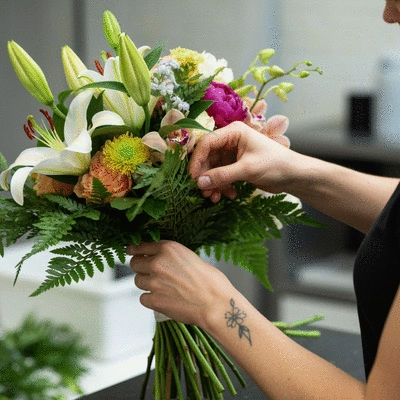 Close-up of a florist's hands arranging a custom bridal bouquet with various flowers and greenery